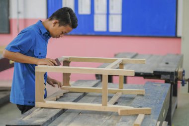 İş kıyafetleri içindeki genç marangoz konsol masasında zımpara kağıdı kullanıyor.