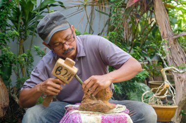 Asyalı bonsai sanatçısı bonsai ağacını yeniden saksılamak için çekiç ve çekiç kullanıyor. Bonsai rock konsepti üzerine