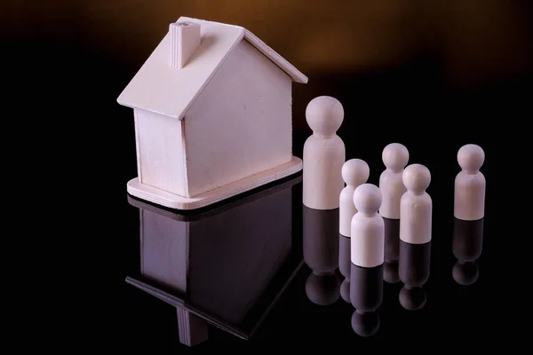 Business, Finance, Home loan and management concept. Close up of wooden people figure standing on glass table with  mini wooden house toy on black background.