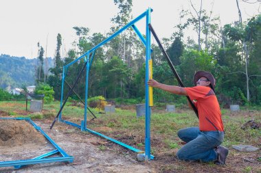Bahçıvanlar bahçede c kanalı çeliğinden bebek odası yapıları inşa ederken kablosuz tornavida ve ruh seviyesini kullanıyorlar..