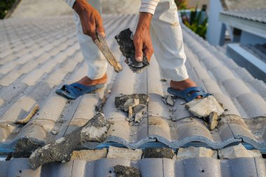 İşçiler hasarlı konutun çatısındaki fayansları onarırken kişisel koruyucu giymezler.