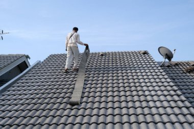 İşçiler hasarlı konutun çatısındaki fayansları onarırken kişisel koruyucu giymezler.