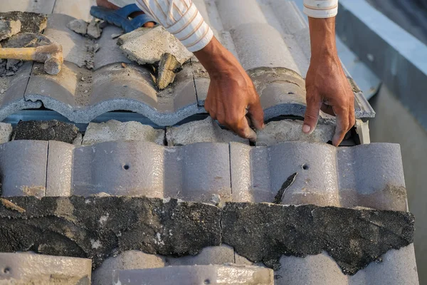 İşçiler hasarlı konutun çatısındaki fayansları onarırken kişisel koruyucu giymezler.