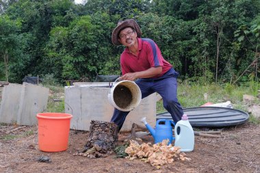 Olgun bir adam meyve bahçesindeki bahçe komposterine mutfak atıkları atıyor. Ev sahibi meyve bahçesindeki atık gübreleriyle geri dönüşümü ayırıyor. Çevre dostu evler kavramı