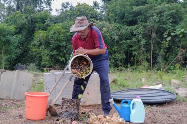 Olgun bir adam meyve bahçesindeki bahçe komposterine mutfak atıkları atıyor. Ev sahibi meyve bahçesindeki atık gübreleriyle geri dönüşümü ayırıyor. Çevre dostu evler kavramı
