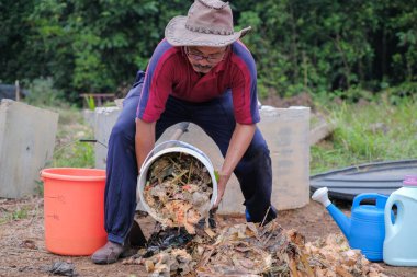 Olgun bir adam meyve bahçesindeki bahçe komposterine mutfak atıkları atıyor. Ev sahibi meyve bahçesindeki atık gübreleriyle geri dönüşümü ayırıyor. Çevre dostu evler kavramı