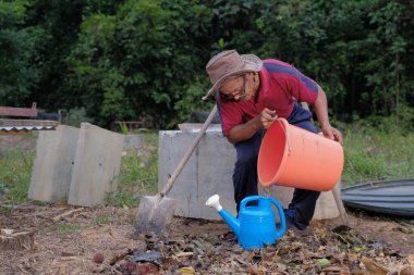 Olgun bir adam, bahçedeki nemli bir süngerin nem oranına ulaşana kadar etkili bir mikro organizmayla gübre yığınına su döker. Çevre dostu evler kavramı