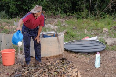 Olgun bir adam, bahçedeki nemli bir süngerin nem oranına ulaşana kadar etkili bir mikro organizmayla gübre yığınına su döker. Çevre dostu evler kavramı