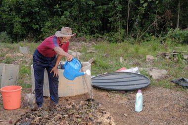 Olgun bir adam, bahçedeki nemli bir süngerin nem oranına ulaşana kadar etkili bir mikro organizmayla gübre yığınına su döker. Çevre dostu evler kavramı