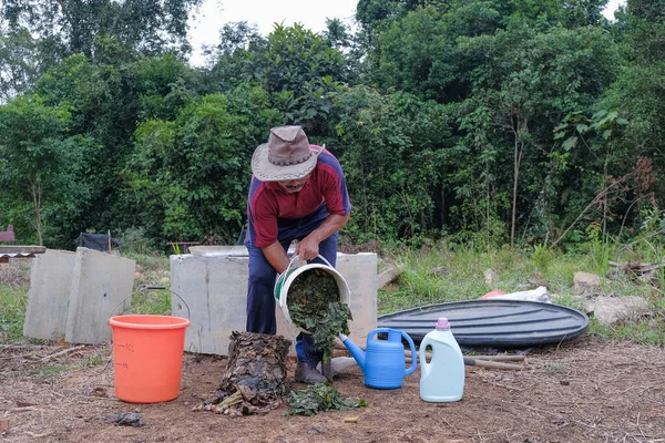 Olgun bir adam meyve bahçesindeki bahçe komposterine mutfak atıkları atıyor. Ev sahibi meyve bahçesindeki atık gübreleriyle geri dönüşümü ayırıyor. Çevre dostu evler kavramı