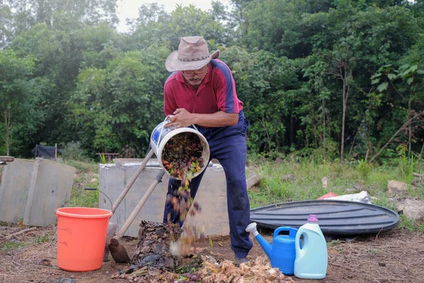 Mature man throwing kitchen waste  into garden composter at orchard .