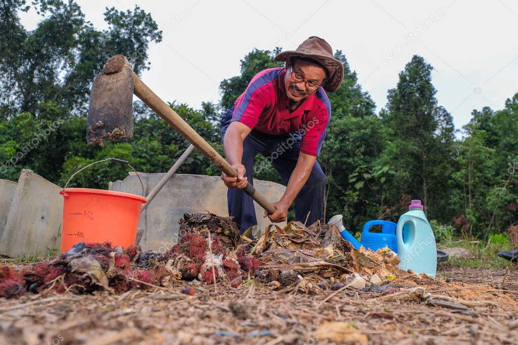 Mature man using a hoe . Male gardener turns,compost heap pile to loosen mixture and aid aeration in the garden. Eco-friendly homes concept