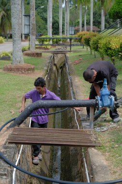 Muadzam Şah, Malezya - 1 Eylül 2021: İki işçi ana drenaja kask veya bot gibi güvenlik ekipmanları olmadan yeni HDPE boruları kuruyor.