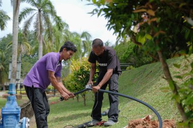 Muadzam Şah, Malezya - 1 Eylül 2021: İki işçi ana drenaja kask veya bot gibi güvenlik ekipmanları olmadan yeni HDPE boruları kuruyor.
