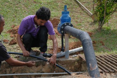 Muadzam Şah, Malezya - 1 Eylül 2021: İki işçi ana drenaja kask veya bot gibi güvenlik ekipmanları olmadan yeni HDPE boruları kuruyor.