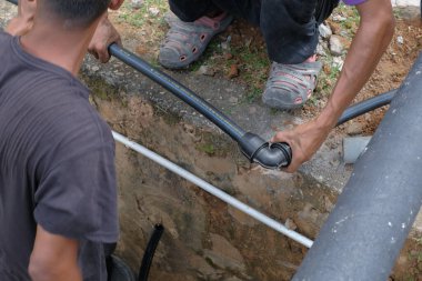 Muadzam Şah, Malezya - 1 Eylül 2021: İki işçi ana drenaja kask veya bot gibi güvenlik ekipmanları olmadan yeni HDPE boruları kuruyor.