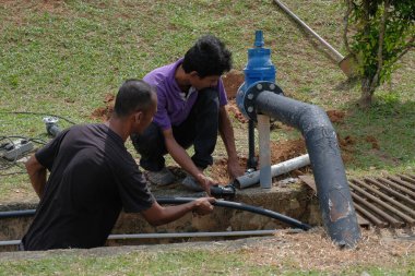 Muadzam Şah, Malezya - 1 Eylül 2021: İki işçi ana drenaja kask veya bot gibi güvenlik ekipmanları olmadan yeni HDPE boruları kuruyor.