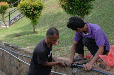 Muadzam Şah, Malezya - 1 Eylül 2021: İki işçi ana drenaja kask veya bot gibi güvenlik ekipmanları olmadan yeni HDPE boruları kuruyor.