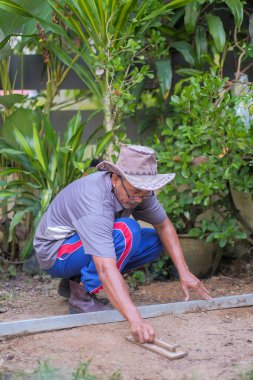 Bahçede çalışan kıdemli bir adam ruh seviyesi, ahşap şamandıra ve düz kenar ile zemini düzleştirir..