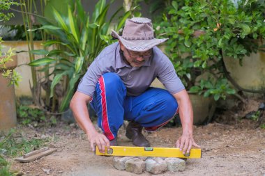 Bahçede çalışan kıdemli bir adam ruh seviyesi, ahşap şamandıra ve düz kenar ile zemini düzleştirir..