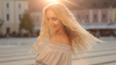 Mutlu ve Gülümseyen Kız 'ın portresi kameranın önünde poz veriyor. Harika görünüyorsun ve saçların çok güzel. Sarışın kadın atlıyor ve dışarıda eğleniyor. Sıcak, güneşli bir akşam.