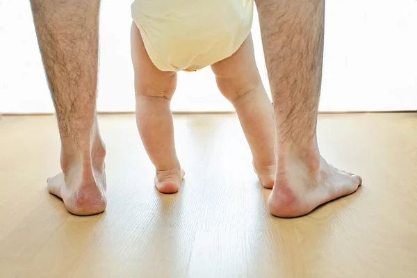 Un bebé está aprendiendo a caminar con sus padres juntos aislados en la pared blanca y el suelo de madera — Foto de Stock