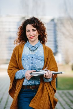 Kıvırcık saçlı kadın dizüstü tutarken street yürüyüş