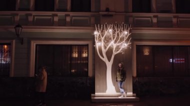 Kız parlak süslü bir Noel ağacının altında sokakta duruyor. tatil görünümleri