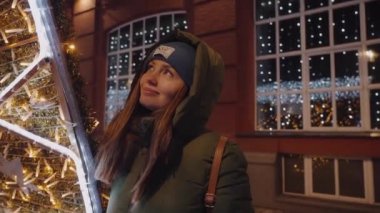 Genç güzel kız sokakta bir çelenge bakıyor. Işık yüzü aydınlatır.