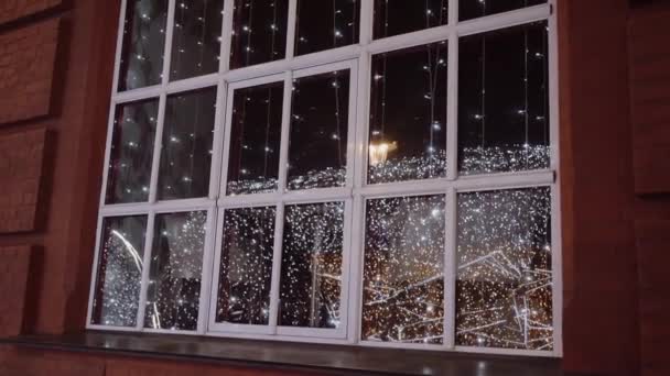 Vakantie kerstverlichting gloeien en worden weerspiegeld in een raam op een gebouw — Stockvideo