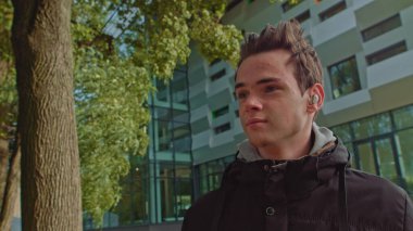 Sokakta yürürken kablosuz kulaklık kullanan genç bir adam. Genç adam, modern kablosuz kulaklık takıyor. Genç bir adamın portresi..