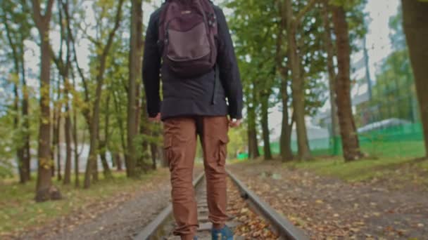 Um jovem bonito de 18 anos em roupas quentes modernas com uma mochila nos ombros caminha na pista, a câmera está fora de foco. O conceito de solidão adolescente, um em todo o mundo — Vídeo de Stock