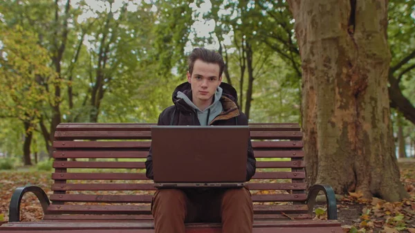 Medium shot van knappe jongeman werken op laptop computer buiten in het park, dan kijkt naar de camera en toont O.K. Werk alleen is ver van het kantoor, freelancer — Stockfoto