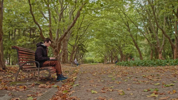 Mladý muž sedí s laptopem v parku. Vážná dospívající, chlap, mladý muž, student pracující na notebooku v parku. Koncept vzdálené práce a učení — Stock fotografie