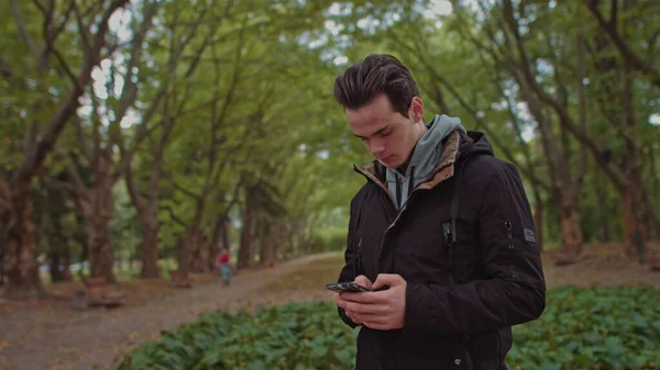 Hipster Man che invia messaggi vocali con il telefono cellulare al parco, studente adolescente usa la ricerca di messaggi audio sull'erba nel parco, tour a piedi zaino in spalla, ricerca vocale — Foto Stock