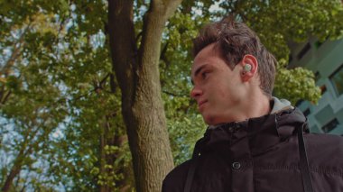 Sokakta yürürken kablosuz kulaklık kullanan genç bir adam. Genç adam, modern kablosuz kulaklık takıyor. Genç bir adamın portresi..