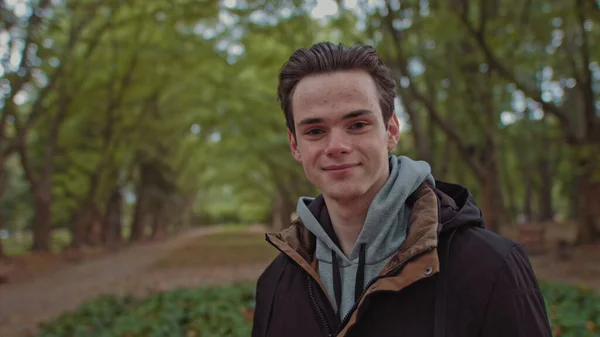 Junger glücklicher Mann blickt in die Kamera. Glücklich lächelndes Männergesicht, draußen. Großaufnahme des Gesichts von Teenagern. Langsam zoomt er auf das Gesicht der Menschen herab. Ein Teenager steht im Park und genießt das Leben. Blick geradeaus — Stockfoto