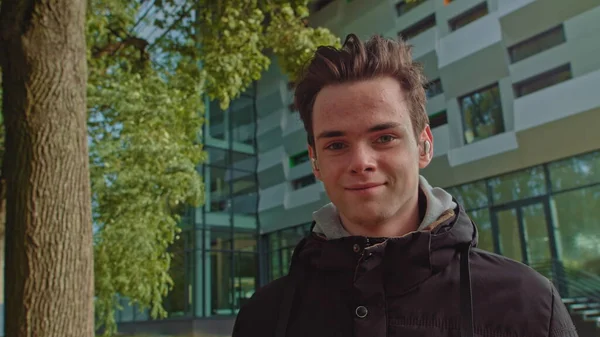 Junger Mann telefoniert mit drahtlosen Kopfhörern im Freien, während er die Straße hinuntergeht. junger Kerl, Teenager trägt moderne drahtlose Kopfhörer. Porträt eines jungen Mannes. — Stockfoto