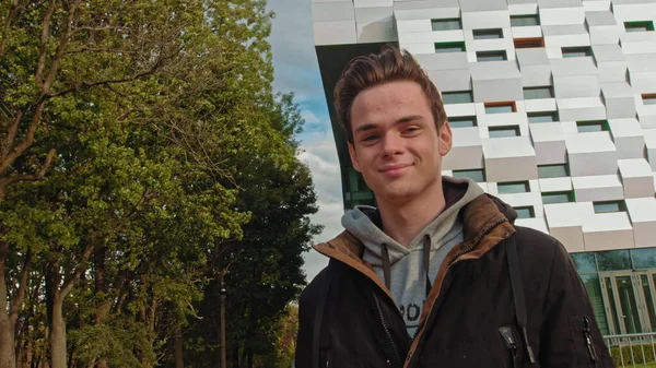 Portrait de jeune homme, adolescent, regardant la caméra et souriant. Portrait d'un adolescent sur le fond d'un centre d'affaires, un bâtiment moderne tout en marchant dans la rue. Au ralenti. Heureux — Photo