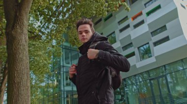 Sırt çantasını takıp kameraya bakan genç bir adamın portresi. Genç bir genç okul ya da üniversite için hazırlanıyor. Kameraya özgüvenli bak. Üniversitenin bölgesindeki adam.