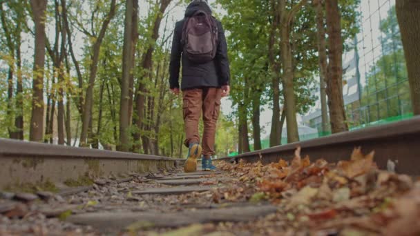 A handsome young man of 18 years in modern warm clothes with a backpack on his shoulders walks on the track, the camera is out of focus. The concept of adolescent loneliness, one in the whole world — Stock Video