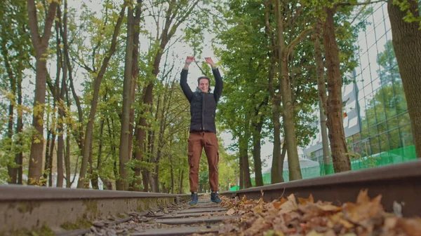 Giocoso uomo felice adolescente, studente, gioisce per il successo. Un giovane ragazzo divertente che rimbalza nel parco e salta con felicità sullo sfondo di un bellissimo tramonto. Al rallentatore. sul davanti — Foto Stock