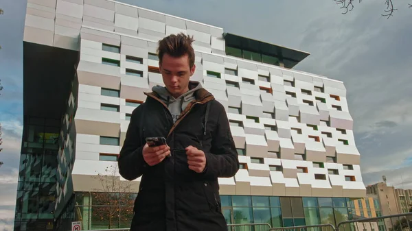 Tenåringer på gaten med en telefon i hendene leser en beskjed om bakgrunnen til en moderne bygning. teknologi, kommunikasjon og livsstilskonsept - unge menn eller tenåringsgutter bruker smarttelefon – stockfoto