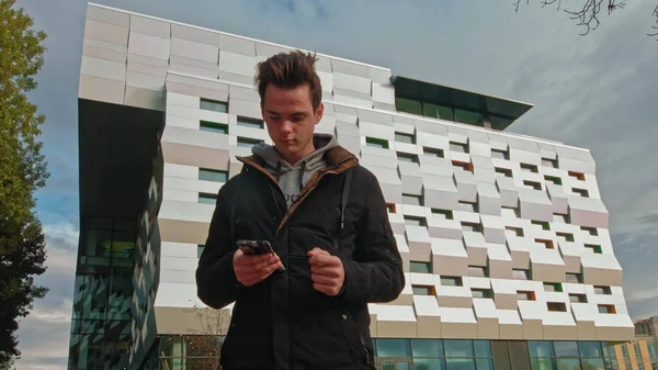 Teini-ikäinen kadulla puhelin kädessään lukee viestin modernin rakennuksen taustalla. teknologia, viestintä ja elämäntapa käsite nuori mies tai teini-ikäinen poika käyttää älypuhelinta — kuvapankkivalokuva