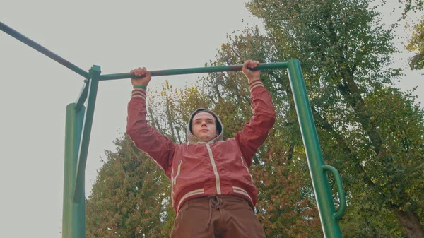 Junge Teenager machen Klimmzugübungen am Reck während des intensiven Trainings im Freien. Der amerikanische Hipster trainiert an einem Frühlingstag allein im Stadtpark. Aktive tragen stylische Kleidung — Stockfoto