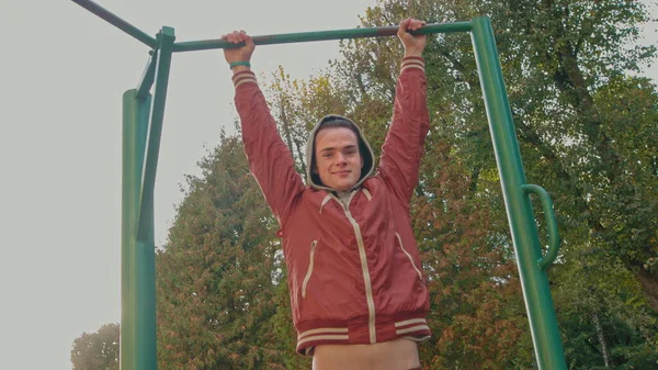Νεαρός έφηβος κάνει ασκήσεις pull ups σε οριζόντια γραμμή κατά τη διάρκεια έντονης άσκησης σε εξωτερικούς χώρους. Ο Αμερικάνος χίπστερ προπονείται μόνος του στο πάρκο την άνοιξη. Ενεργό άτομο με στυλ — Φωτογραφία Αρχείου