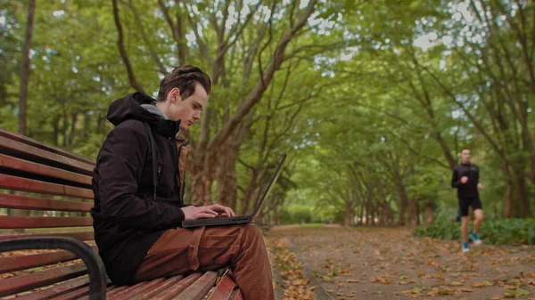 Young man sitting with a laptop in the park .serious teenage, guy, young man, student working on laptop in the park. Remote work and learning concept — Stock Photo, Image