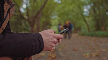 Elinde telefonla parkta bir bankta oturan genç bir adam. Arka planda, parkta yürüyen bir grup arkadaş. Yalnızlık ve internet ve akıllı telefonlara bağımlılık kavramı..