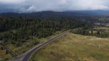 Gün doğumunda sisle kaplı bir dağ yoluna inen hava manzarası.