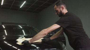 Kadın ve erkek arabayı temizler. Adam özel bir bezle yıkadıktan sonra arabanın kaputunu siliyor.